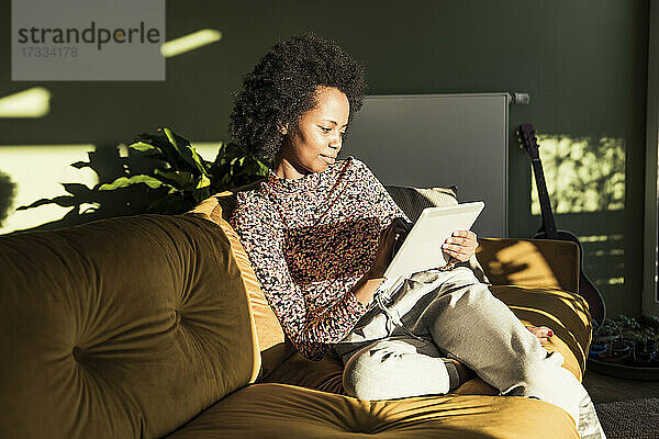 Frau benutzt digitales Tablet  während sie auf dem Sofa im Wohnzimmer sitzt