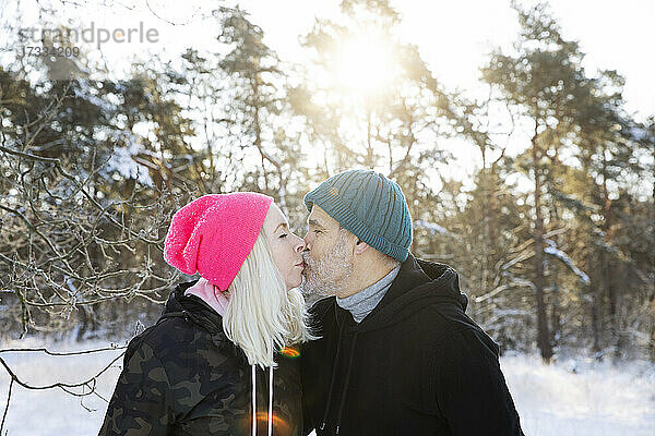 Paar mit Strickmützen  das sich im Winter küsst