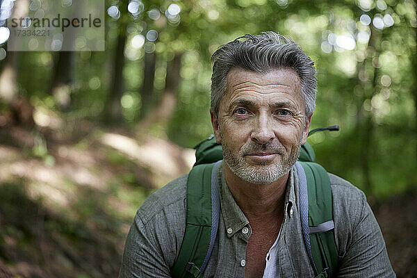 Lächelnder gutaussehender männlicher Wanderer mit Rucksack im Wald
