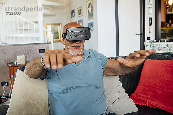 Mann gestikuliert  während er eine Virtual-Reality-Brille zu Hause trägt