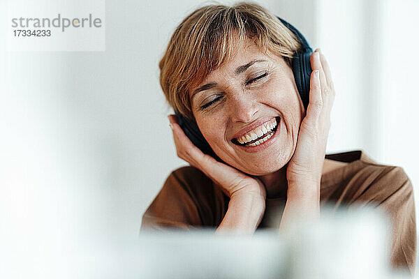 Reife Geschäftsfrau lächelnd beim Hören von Musik über Kopfhörer im Büro