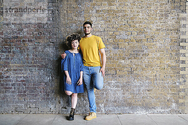 Junges Paar steht zusammen auf einem Bein vor einer Wand