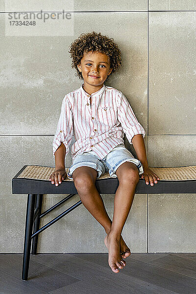 Niedlicher Junge sitzt lächelnd auf einer Bank
