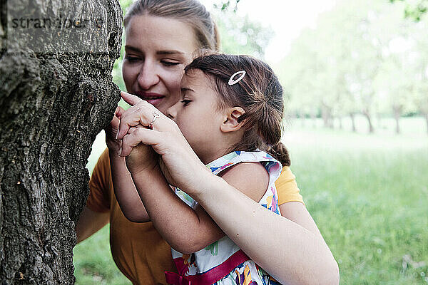 Mutter und Tochter berühren einen Baumstamm im Park
