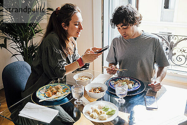 Freundin fotografiert Essen mit dem Mobiltelefon  während sie mit ihrem Freund zu Hause zu Mittag isst