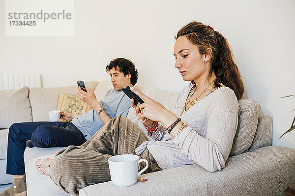 Ein Paar benutzt ein Mobiltelefon  während es zu Hause auf dem Sofa sitzt