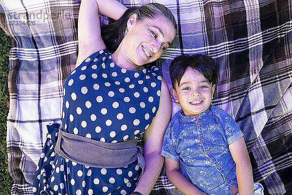 Lächelnde reife Frau sieht ihren Enkel an  während sie sich auf einer Decke ausruht