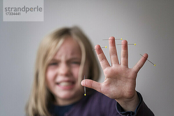 Mädchen zeigt Hand mit Nadeln durchbohrt in der Haut gegen grauen Hintergrund
