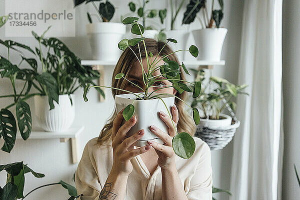 Frau hält Zimmerpflanze vor dem Gesicht zu Hause