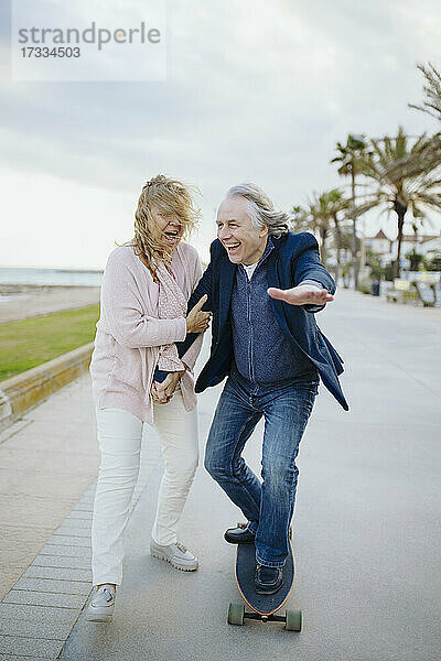Älterer Mann genießt das Skateboardfahren mit einer Frau  die zu Fuß unterwegs ist und die Hände hält