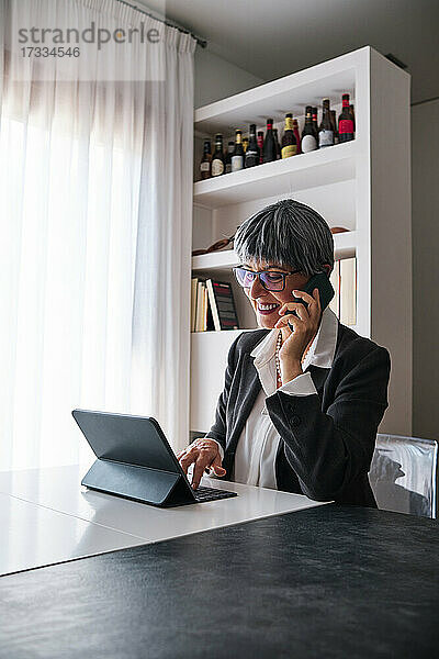 Geschäftsfrau mit digitalem Tablet  die zu Hause mit ihrem Smartphone telefoniert