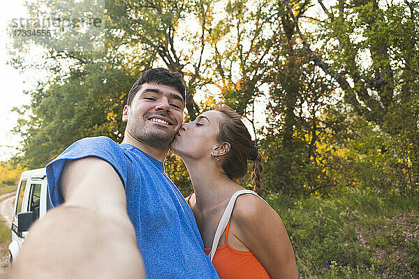Frau küsst Freund bei Selfieaufnahme im Wald