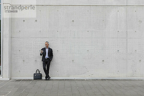 Männlicher Berufstätiger  der ein Smartphone benutzt  während er an einer Wand steht