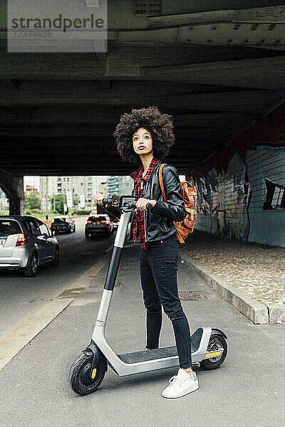 Junge Frau mit Elektroroller auf der Straße unter einer Brücke stehend