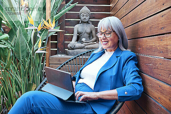Reife Geschäftsfrau  die ein digitales Tablet benutzt  während sie auf einem Stuhl sitzt
