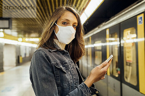 Frau mit Gesichtsmaske hält Mobiltelefon in der U-Bahn
