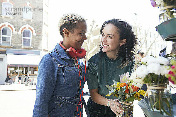 Lächelndes lesbisches Paar  das sich beim Kauf eines Blumenstraußes auf dem Markt gegenseitig anschaut