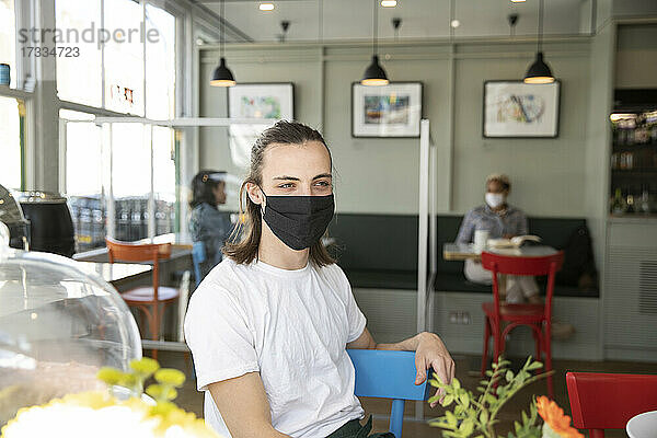 Männlicher Café-Besitzer mit Gesichtsschutzmaske  der wegschaut  während er während der Pandemie im Café sitzt