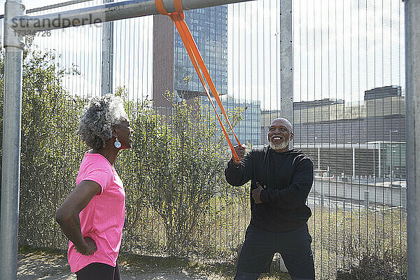 Lächelnder Mann  der an einem Widerstandsband zieht  während er mit einer älteren Frau im Park trainiert