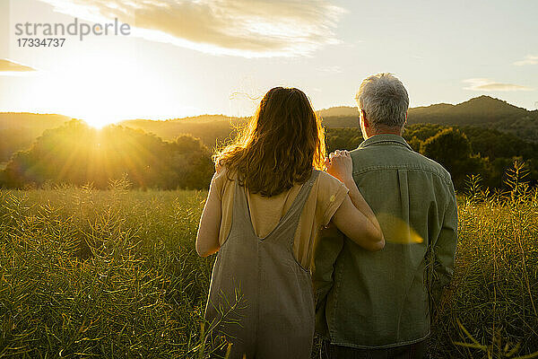 Tochter und Vater betrachten den Sonnenuntergang  während sie in einem Feld stehen