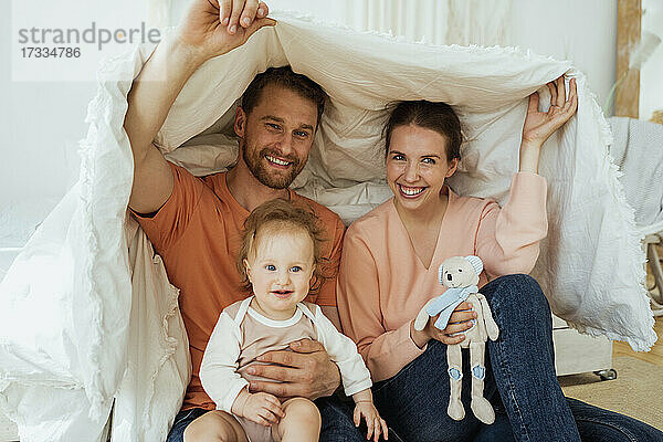 Lächelnder Mann und lächelnde Frau mit einer in eine Decke gehüllten Tochter zu Hause