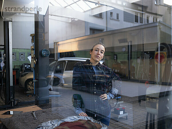Weiblicher Mechaniker in einer Autowerkstatt durch ein Fenster gesehen