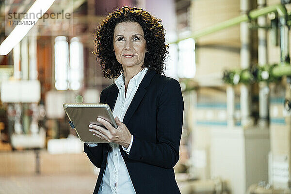 Selbstbewusste Geschäftsfrau  die ein digitales Tablet hält  während sie in der Industrie steht