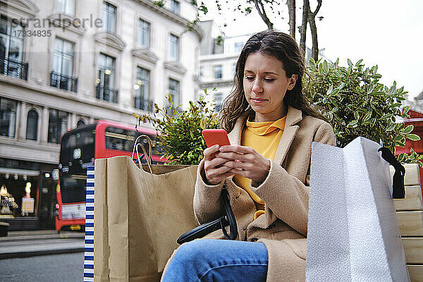 Junge Frau mit Einkaufstüten und Smartphone in der Stadt