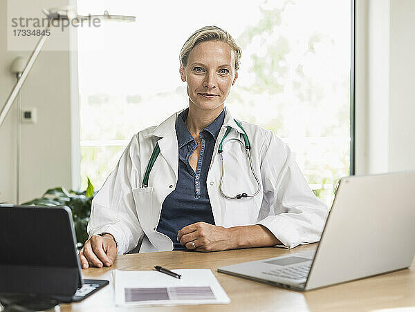 Ärztin mit Laptop und digitalem Tablet im Büro sitzend