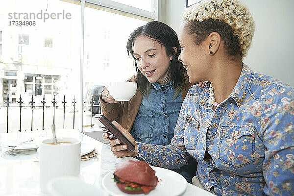 Frau teilt Smartphone mit Freundin beim Kaffeetrinken im Café