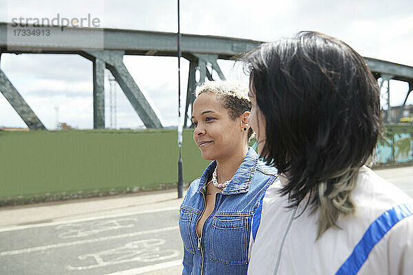 Lesbische Frau sieht ihre Freundin an  während sie zusammen auf einer Brücke spazieren gehen