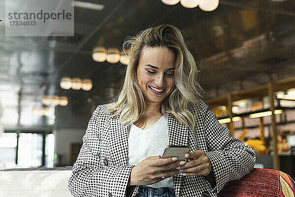 Lächelnde Geschäftsfrau mit blondem Haar  die in einem Café ihr Smartphone benutzt