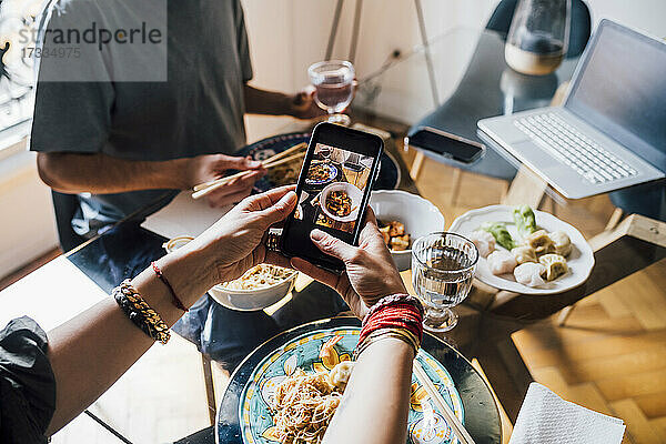Frau fotografiert Essen durch Smartphone mit Mann im Hintergrund am Esstisch