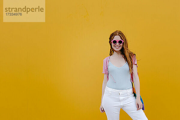 Lächelnde junge Frau vor einer Wand stehend