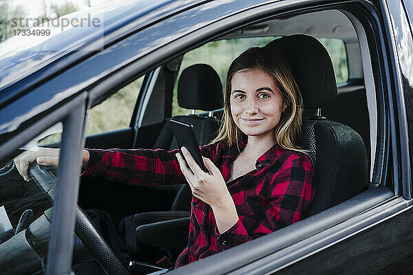 Lächelnde schöne Frau mit Smartphone im Auto sitzend