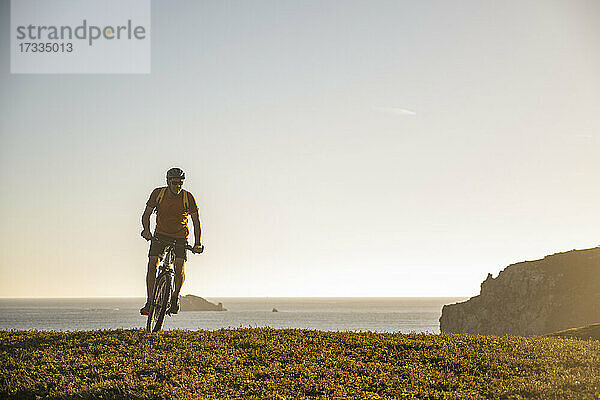 Männlicher Sportler fährt Mountainbike auf einer Wiese bei Sonnenuntergang