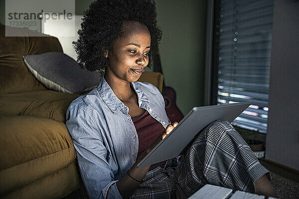Lächelnde Frau  die ein digitales Tablet benutzt  während sie im Wohnzimmer sitzt