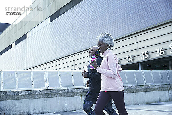Ältere Frau hält Wasserflasche beim Laufen mit Mann in der Stadt