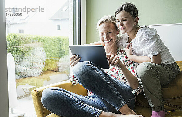 Lächelnde Mutter und Tochter benutzen ein digitales Tablet  während sie auf dem Sofa sitzen