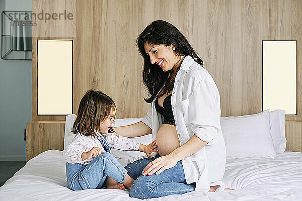 Nettes Mädchen berühren schwangere Mütter Bauch  während auf dem Bett zu Hause sitzen