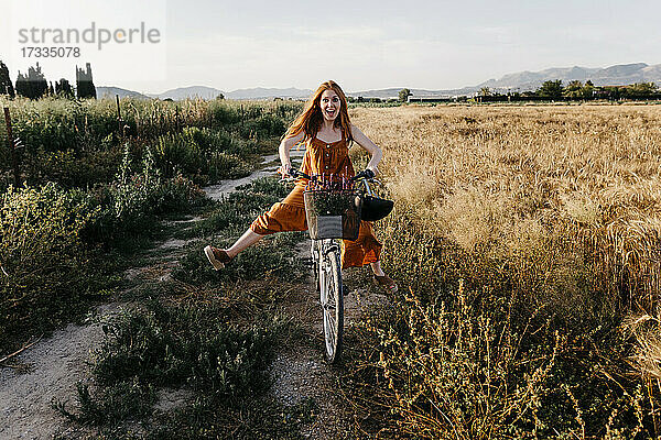 Unbekümmerte Frau fährt Fahrrad in einem landwirtschaftlichen Feld