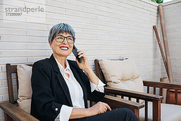 Reife Geschäftsfrau mit Brille  die im Hinterhof mit einem Smartphone telefoniert