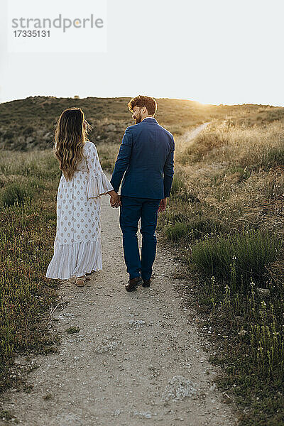 Paar hält sich an den Händen  während es gemeinsam bei Sonnenuntergang spazieren geht