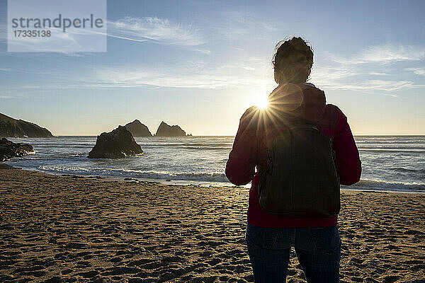 Frau mit Rucksack bei Sonnenuntergang am Strand stehend