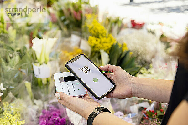 Frau hält Smartphone beim kontaktlosen Bezahlen im Blumenladen