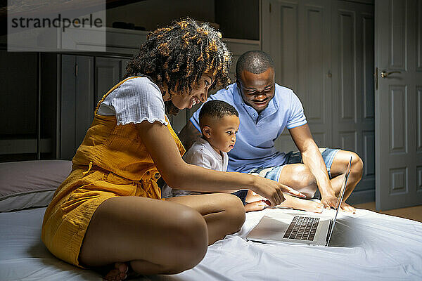 Multiethnische Familie mit Laptop auf dem Bett im Dachgeschoss zu Hause