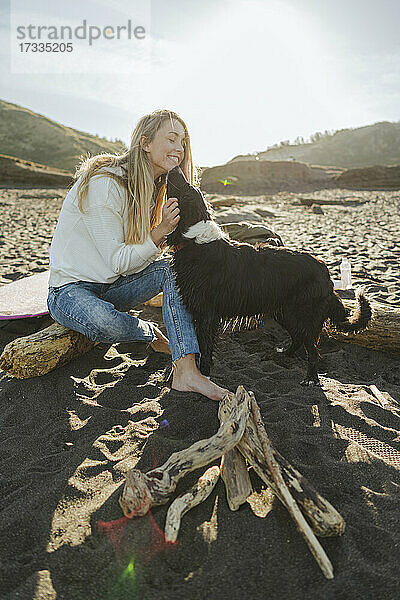 Hund leckt glückliche blonde Frau am Strand