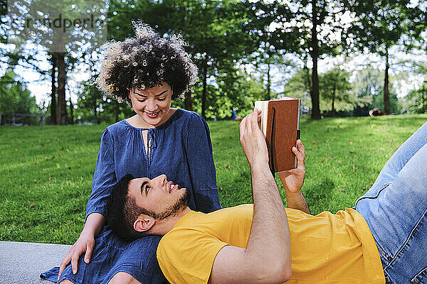 Lächelnde junge Frau sieht ihren Freund auf dem Schoß liegend im Park an