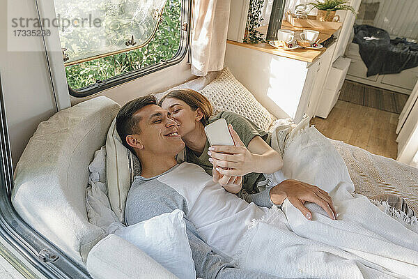 Frau küsst Freund und macht Selfie auf dem Bett im Wohnmobil
