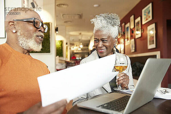 Ältere Geschäftsfrau hält ein Getränk in der Hand und sieht einen männlichen Kollegen im Restaurant an